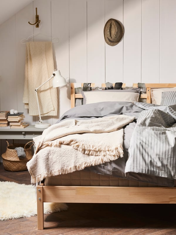 Une chambre confortable dans des tons et des matériaux terreux. Le lit en bois est recouvert de plusieurs couches de textiles. À l'arrière, les panneaux de bois blanc sont visibles.