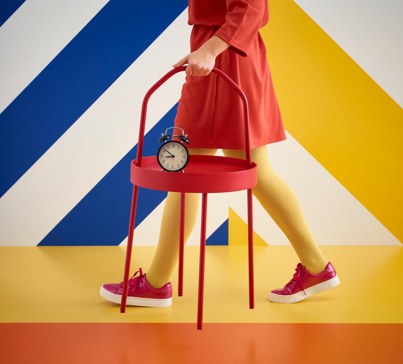 A woman in red dress is walking with a red BURVIK table in her hand.