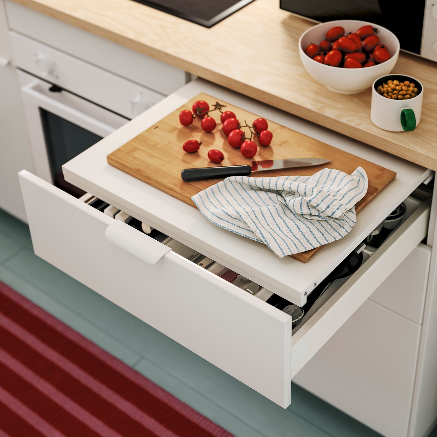 A white UTRUSTA pull-out work surface with a cutting board, tomatoes, and a checkered cloth in a modern kitchen setting.