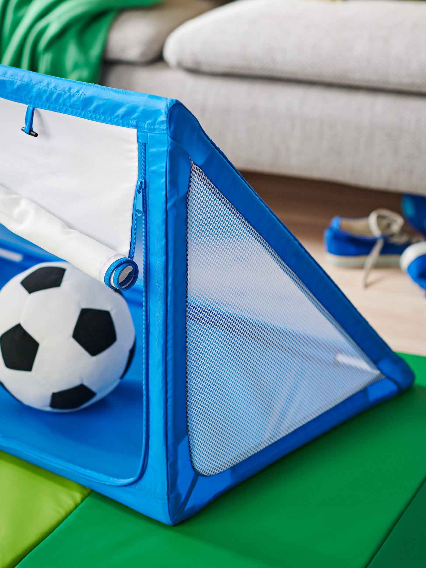 Un living con un arco de fútbol SPORTSLIG azul de IKEA sobre una colchoneta infantil.