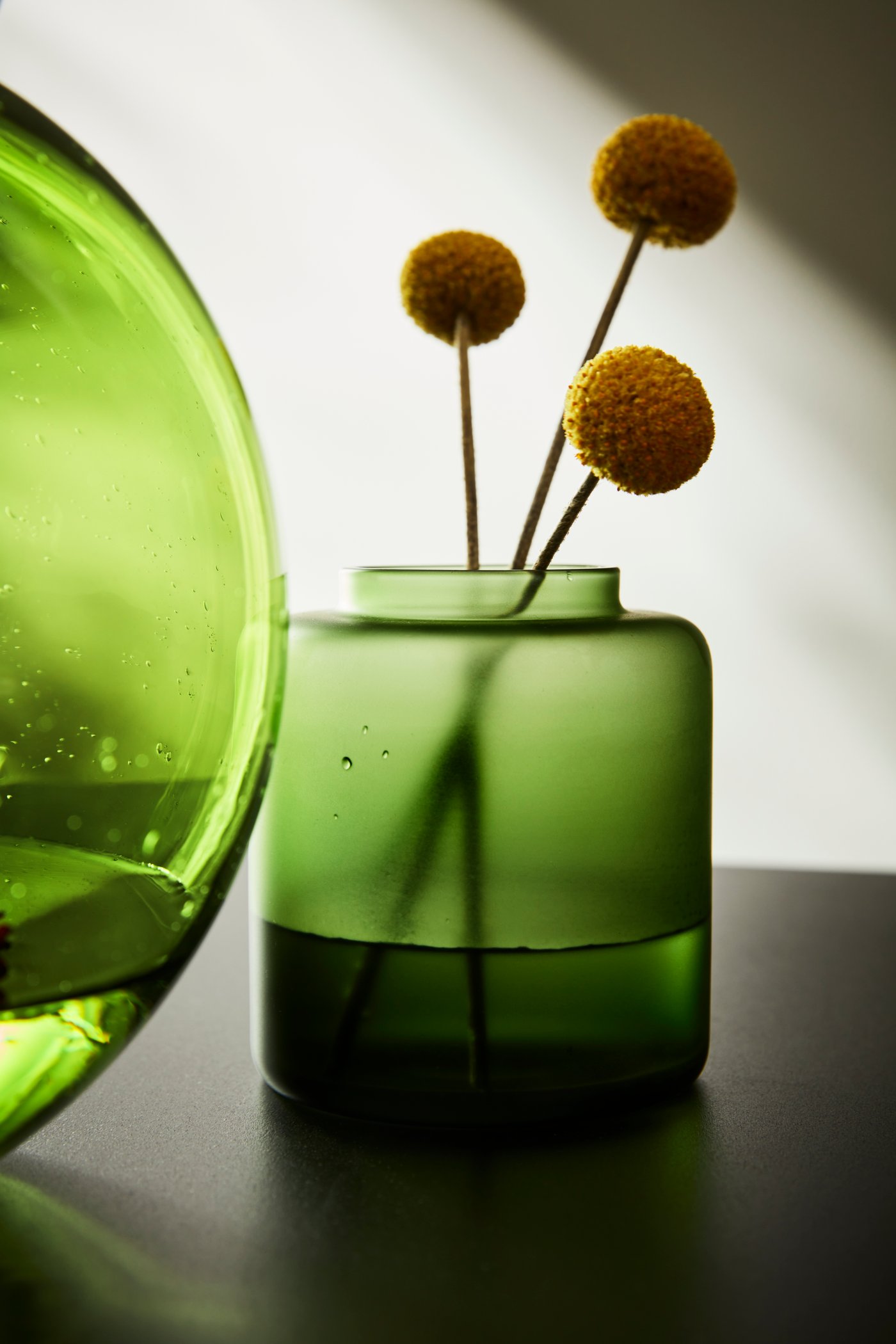 Un vase vert transparent avec des fleurs séchées aux pétales sphériques
