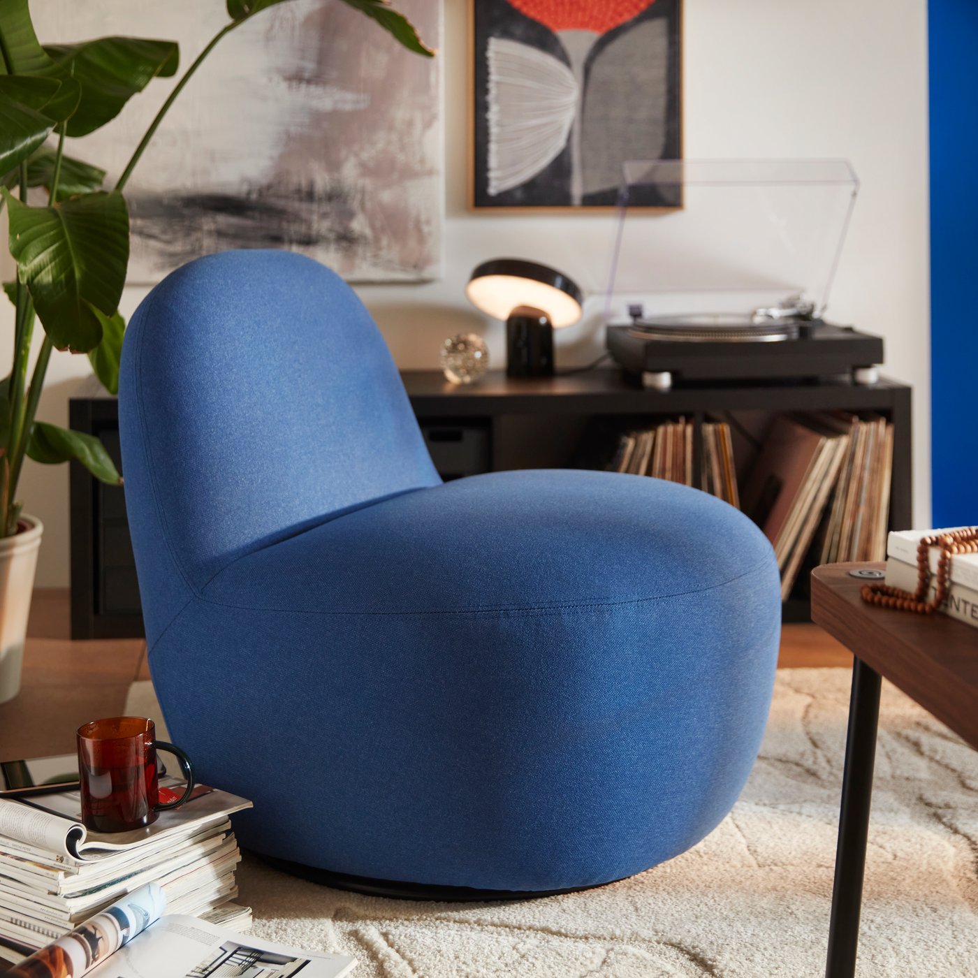 A living room features a Gunnared dark blue LILLESÄTER swivel easy chair made of fabric, beside a plant and a record player.