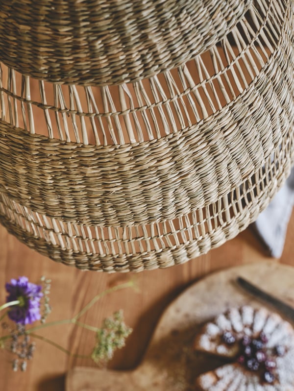 A large TORARED pendant lamp hangs abobe a wooden table with houseplants below.