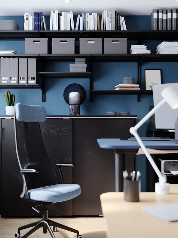Un bureau avec un rangement GALANT brun foncé, et plusieurs tablettes de rangement sur le mur contenant des articles d’organisation pour bureau.
