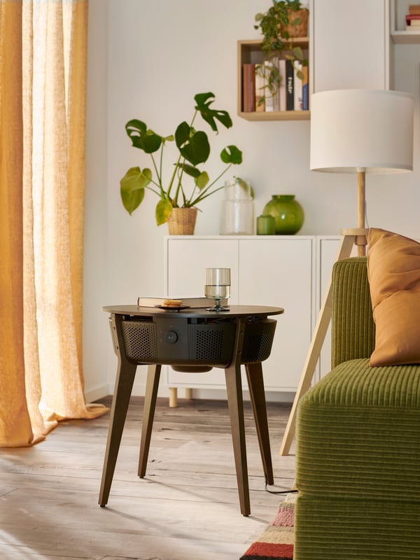 Une table STARKVIND au placage chêne teinté brun foncé avec un purificateur d’air est placée à côté d’un canapé JÄTTEBO dans un salon au plancher en bois.