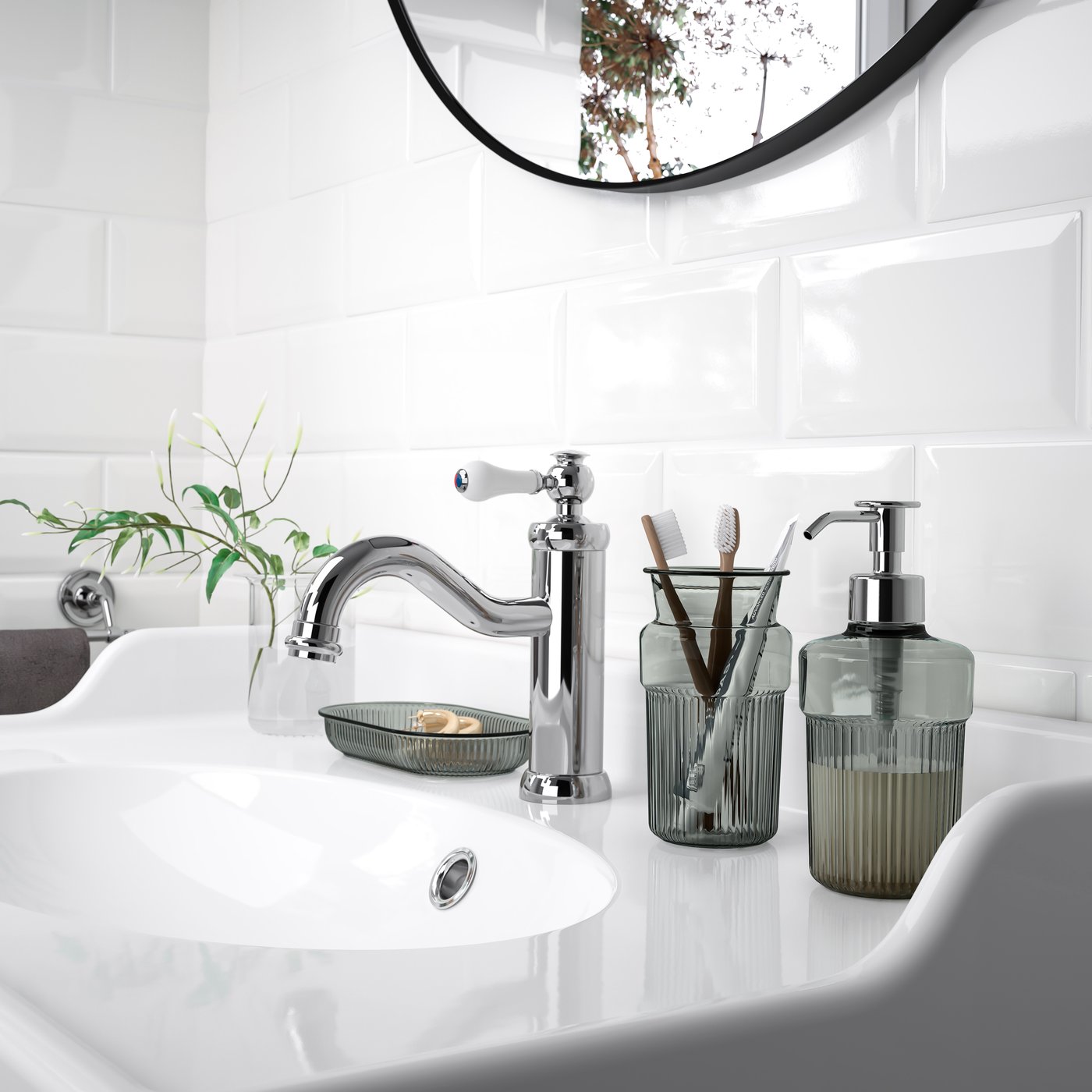 BROFJÄRDEN soap dispenser, toothbrush holder, and soap dish in smoked glass look on white sink against white tiles.