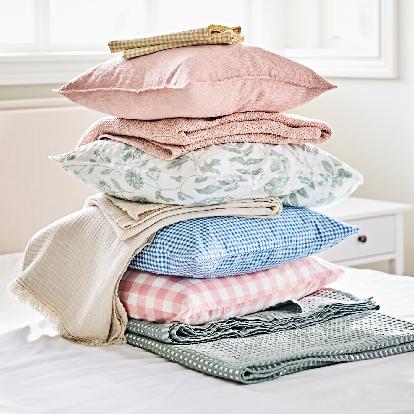 Des oreillers, des jetés et des housses de couette, de couleurs et de motifs différents, sont empilés sur un lit dans une chambre.