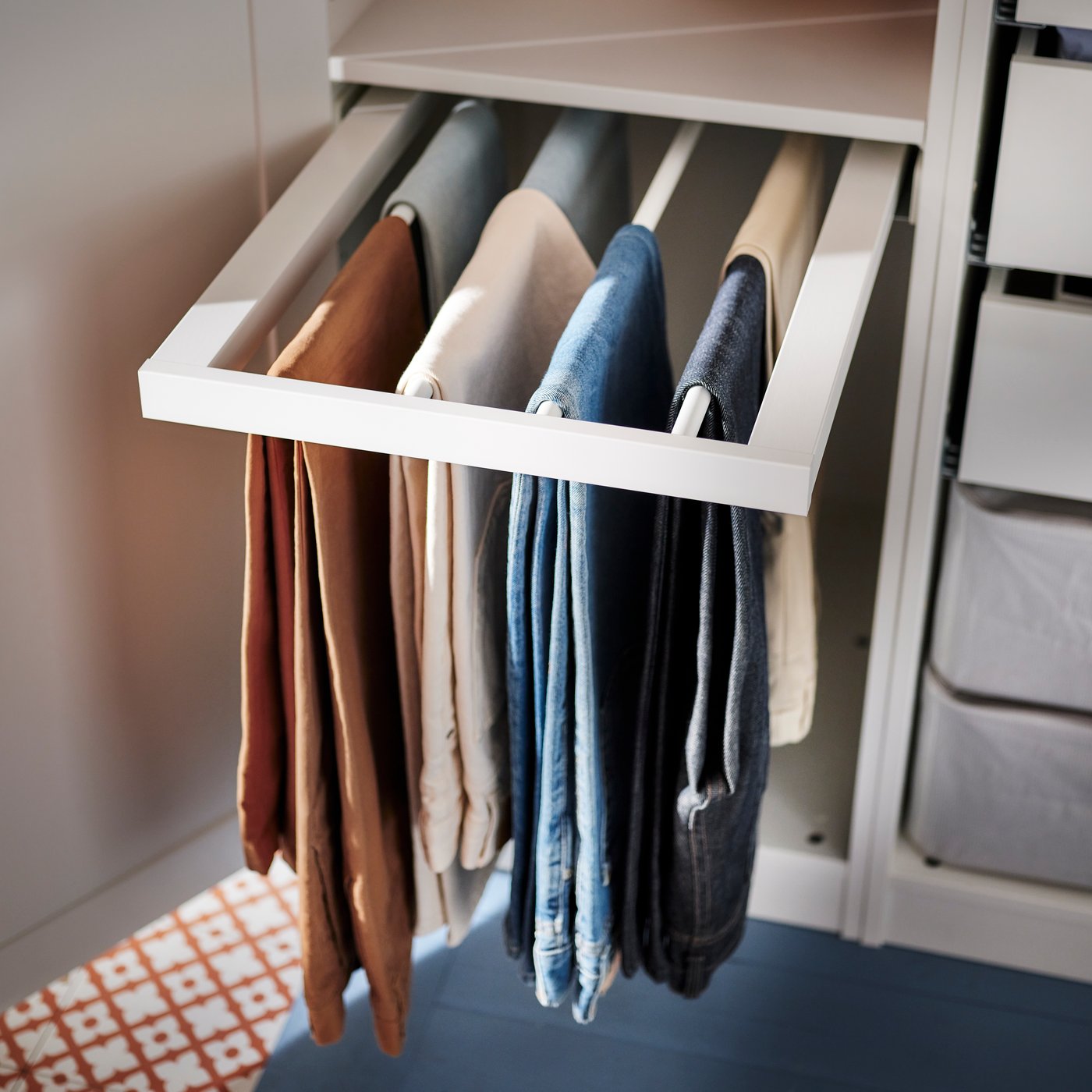 A KOMPLEMENT pull-out trouser hanger holding several pairs of trousers that’s pulled out from inside a PAX/TYSSEDAL wardrobe.