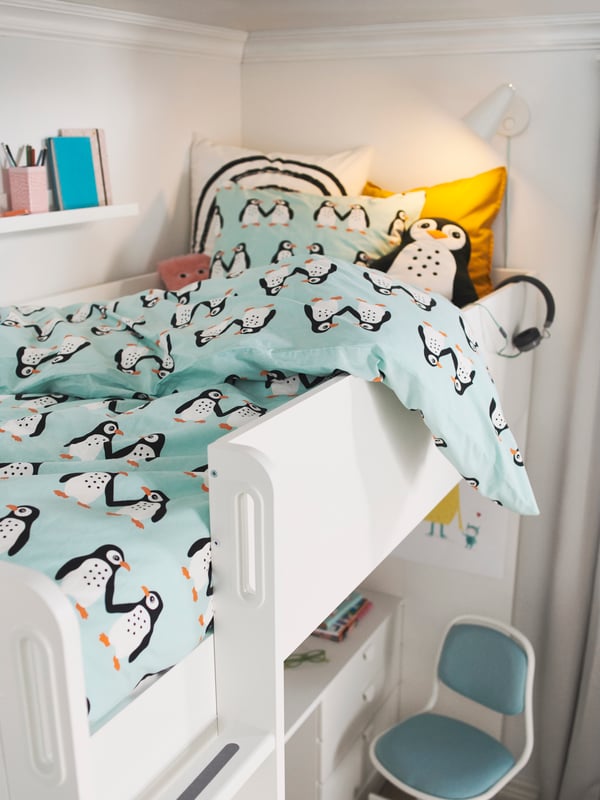 A KURA reversible bed with BLÅVINGAD bed linen with a penguin pattern stands in a bedroom on a yellow LANGSTED rug.