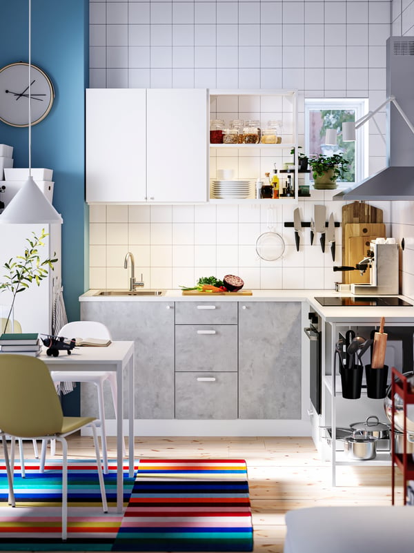 A kitchen with ENHET kitchen cabinets, a table and chairs on a colourful rug and a white pendant lamp above.