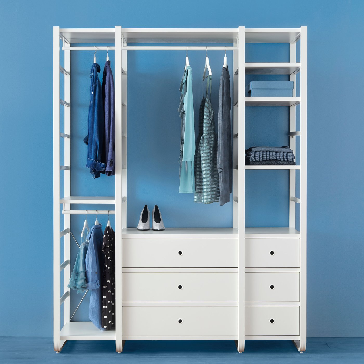 Eine ELVARLI Kleiderschrankkombination in einem blauen Raum. An einer Stange hängen Kleidungsstücke, ansonsten sind noch Taschen und andere Gegenstände zu sehen.