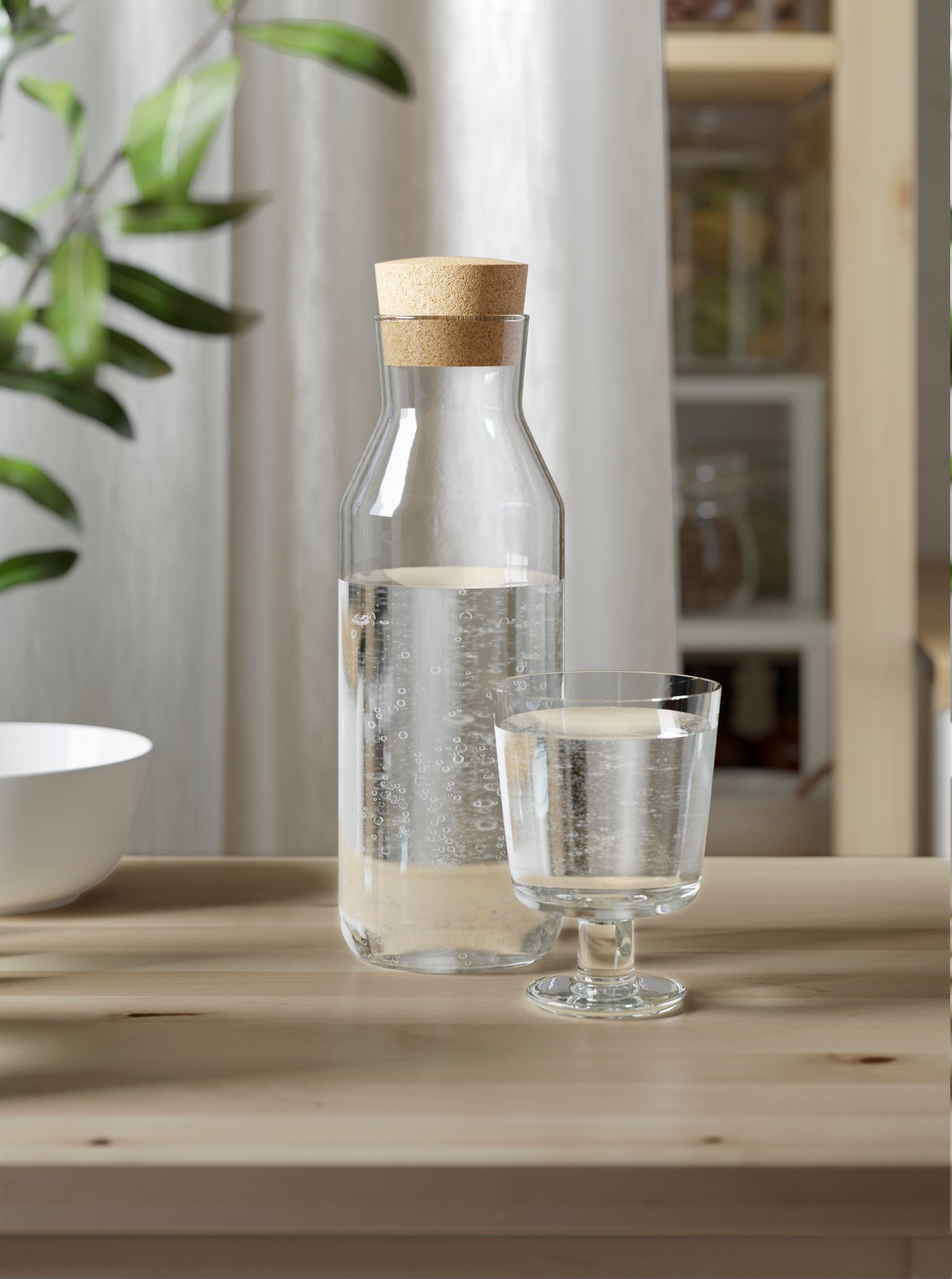 A clear glass IKEA 365+ goblet and a jar with cork lid on a dining table.