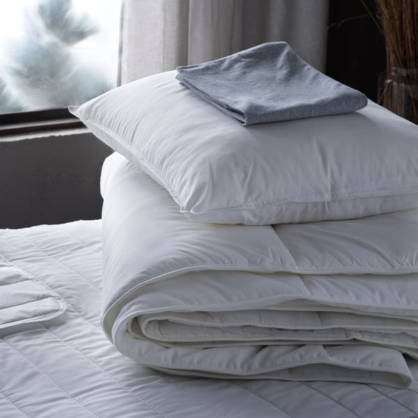 A folded pillowcase lies on top of a pillow which is on top of a folded SMÅSPORRE duvet on a bed near a window.