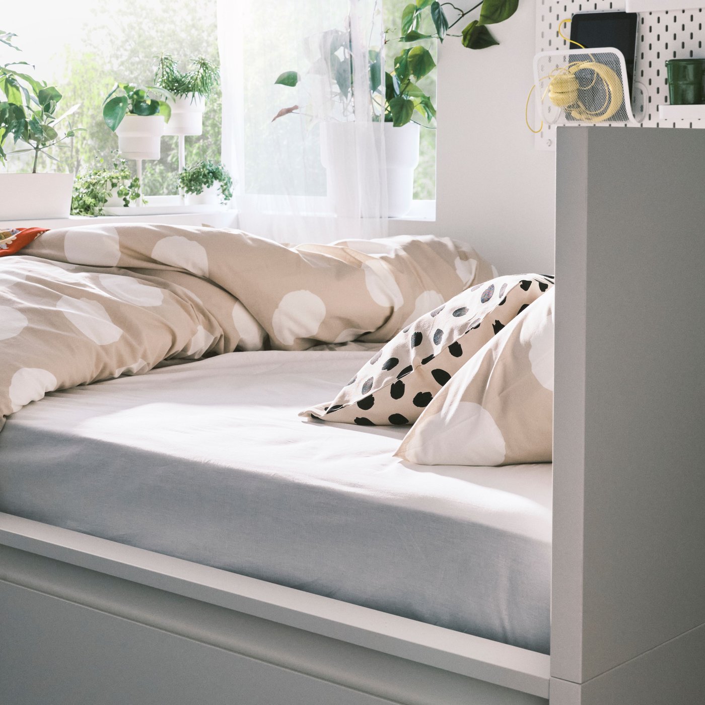 Sur un lit MALM blanc, linge de lit KLYNNETÅG beige/blanc/à pois et coussin avec housse ODDNY blanc cassé/à pois noirs.