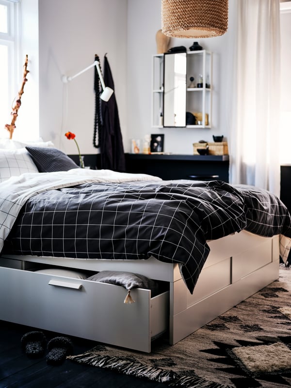 Cama con almacenaje BRIMNES color gris, en un dormitorio de paredes blancas. La cama tiene una funda de plumón VITKLÖVER.