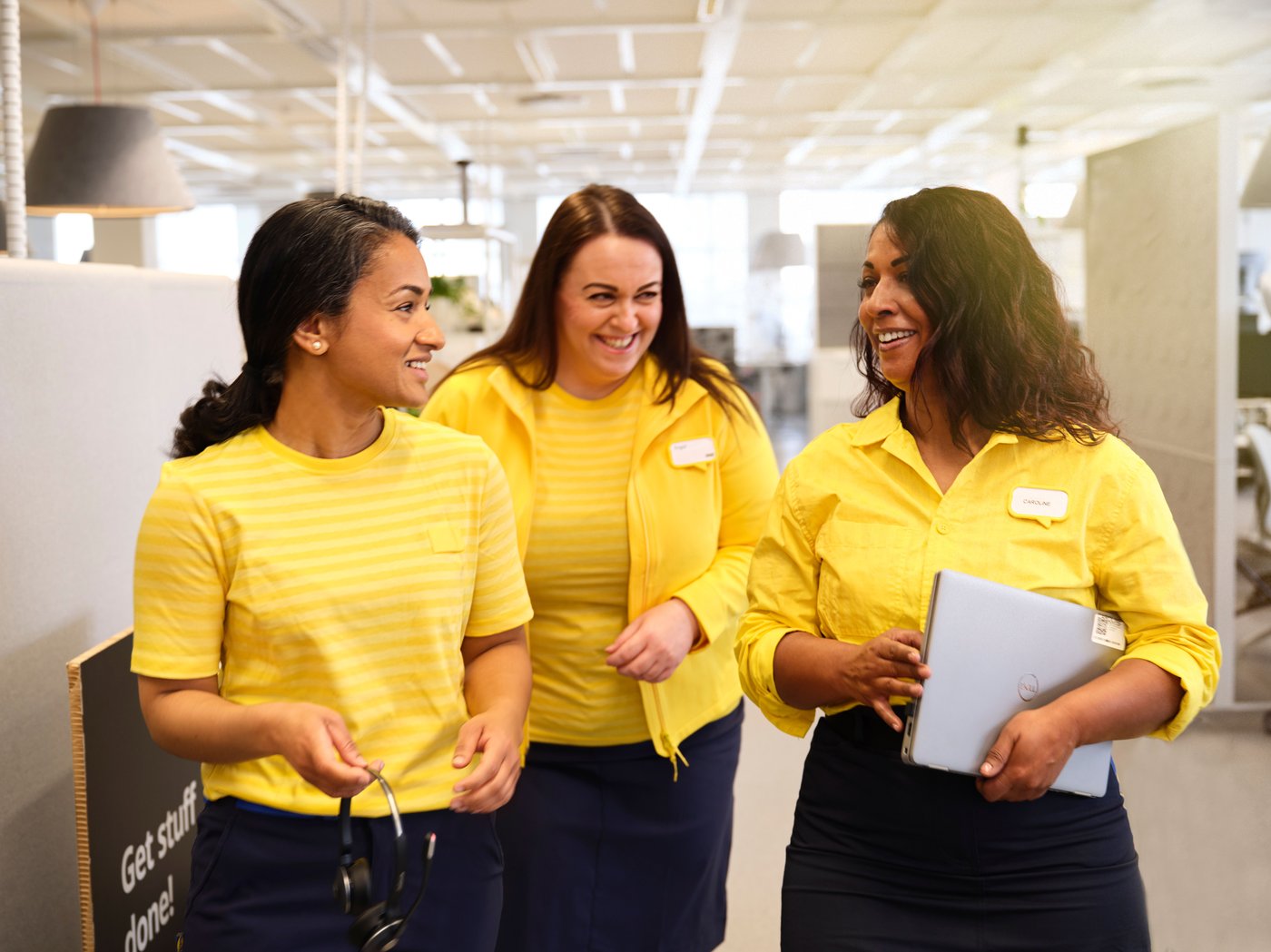 Tre IKEA medarbejdere i gul IKEA trøje går og snakker og smiler