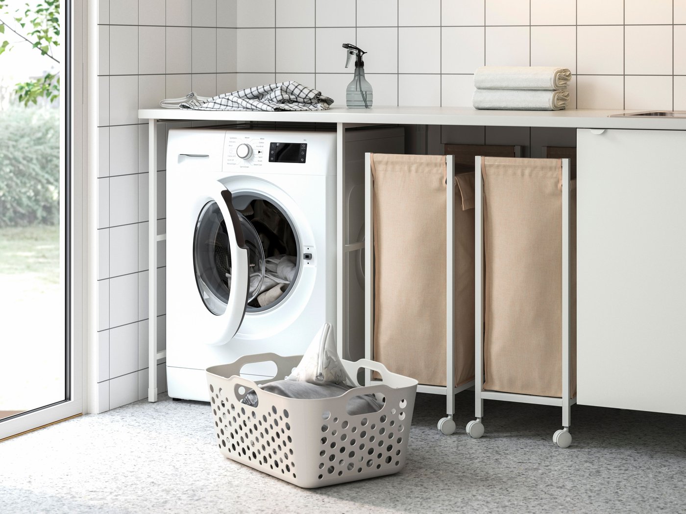 Tvättstuga med tvättmaskin, tvättkorg och två tvättsorterare under arbetsbänk.