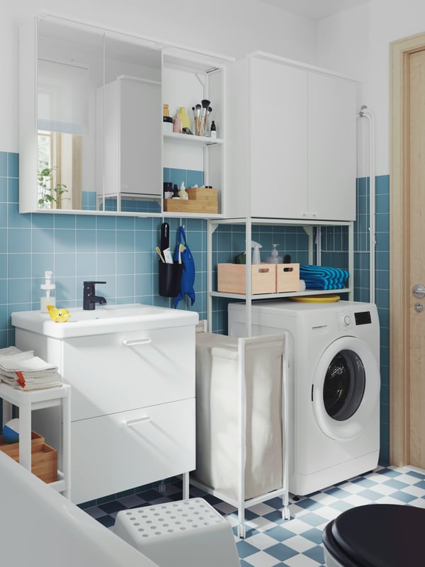 A bathroom has a white ENHET base cabinet, a wall cabinet with mirror doors and a frame with shelves for washing machine.