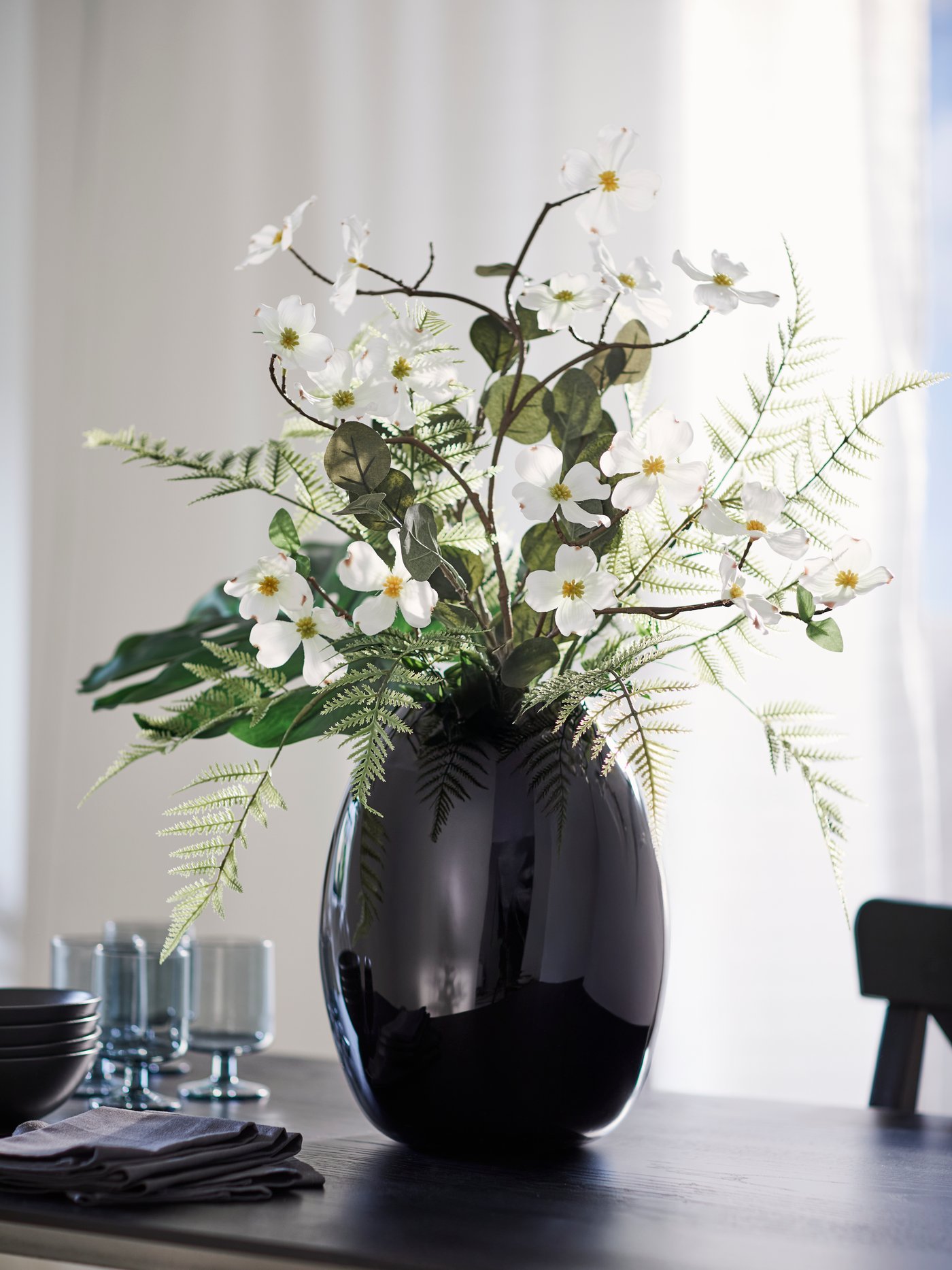 A bouquet of artificial leaves, artificial ferns and a white dogwood SMYCKA artificial spray in a STOCKHOLM 2025 vase.