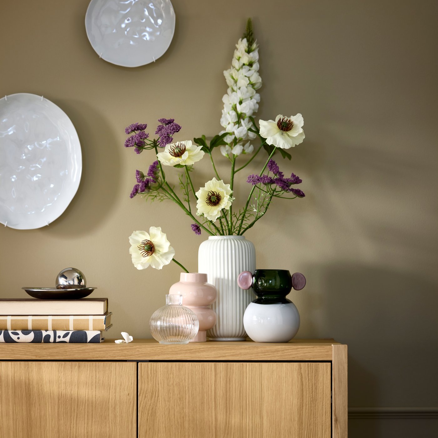 Neatly arranged SMYCKA artificial flowers in a vase flanked by other decoration on top of a STOCKHOLM wooden cabinet.