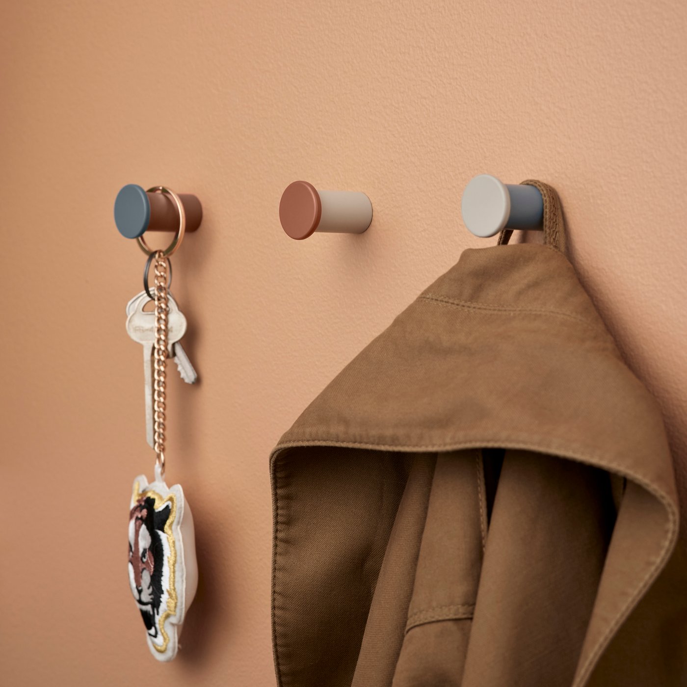 Three wall hooks with a jacket hanging on one and a set of keys hanging on another