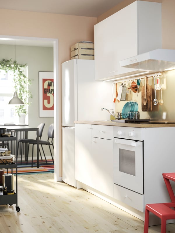 A white KNOXHULT kitchen with base cabinets and a wall cabinet, a fridge and freezer and a dining area in the background.
