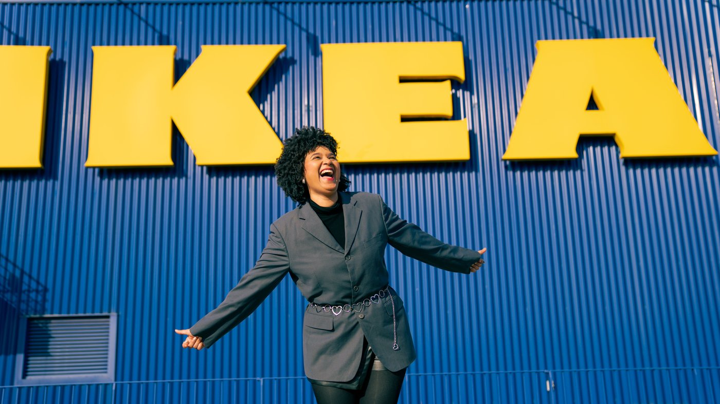 Person står poserande framför en blå fasad med stora gula IKEA‑bokstäver på byggnaden.