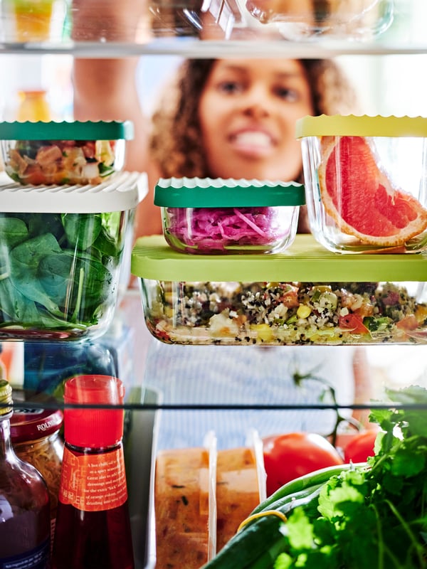 Una mujer abre una nevera con diferentes contenedores de alimentos de vidrio con tapas plásticas.