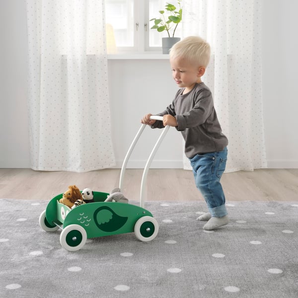 A small child is walking with a green UPPSTÅ toddler walker.