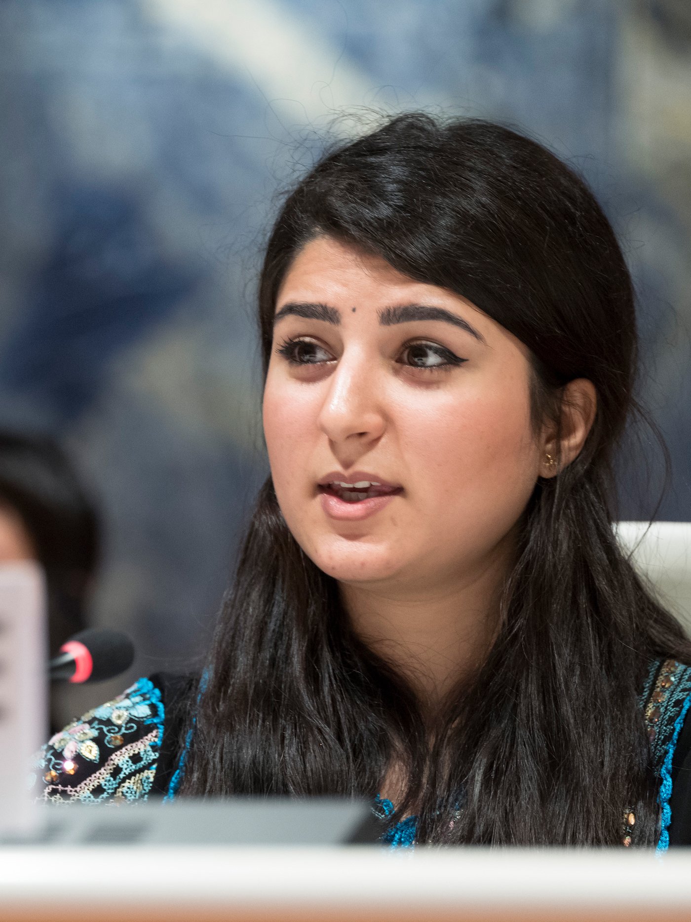 Portræt af en irakisk flygtning, Aya Abdullah, der står og taler på et podium.
