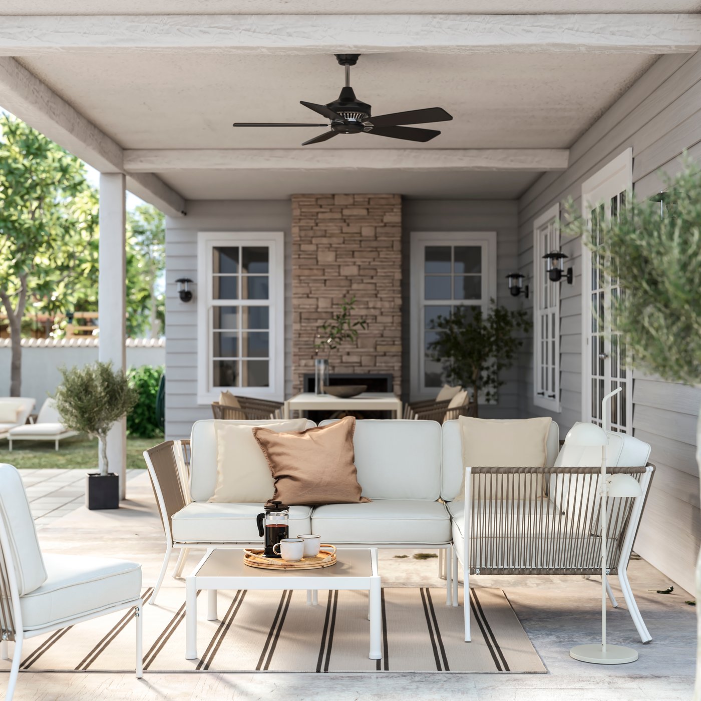 Lounge esterno SEGERÖN bianco su patio con tappeto a righe, tavolino, ventilatore a soffitto e camino in pietra.