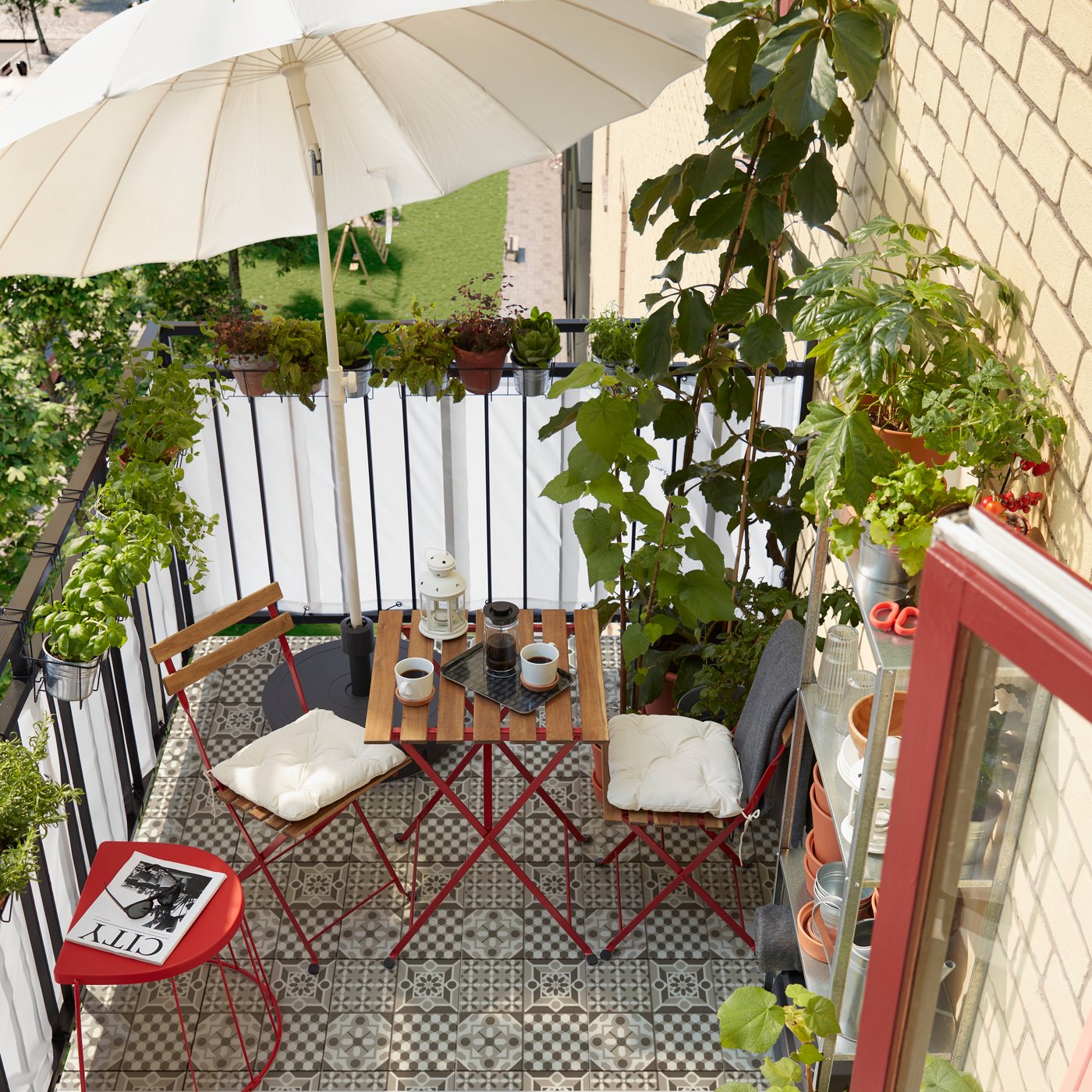 Un pequeño balcón con muchas hierbas y plantas, una estantería con macetas, un parasol, dos sillas y una mesa.