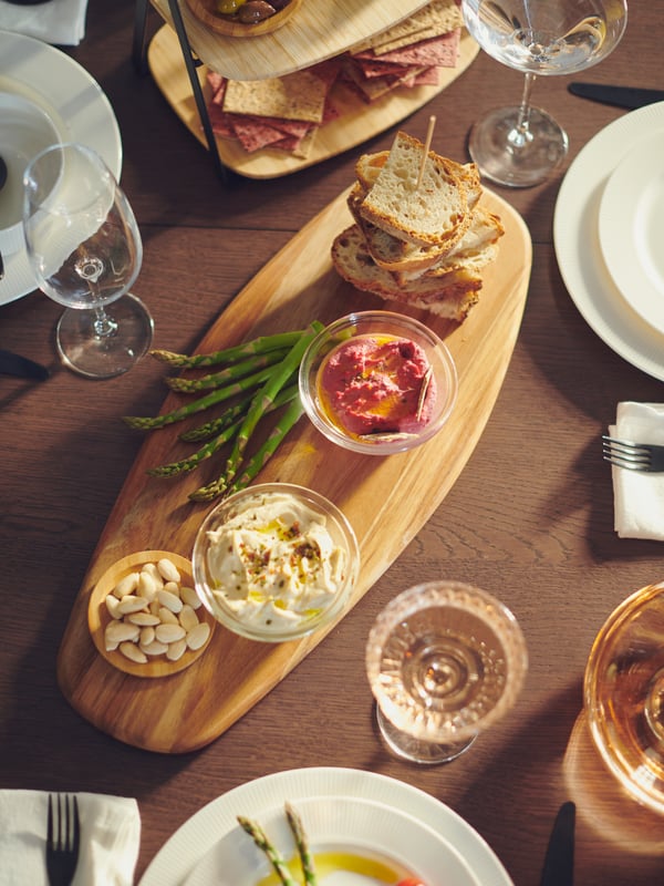 A FASCINERA chopping board with small glass bowls containing various items of food on it, and other glasses and tableware.
