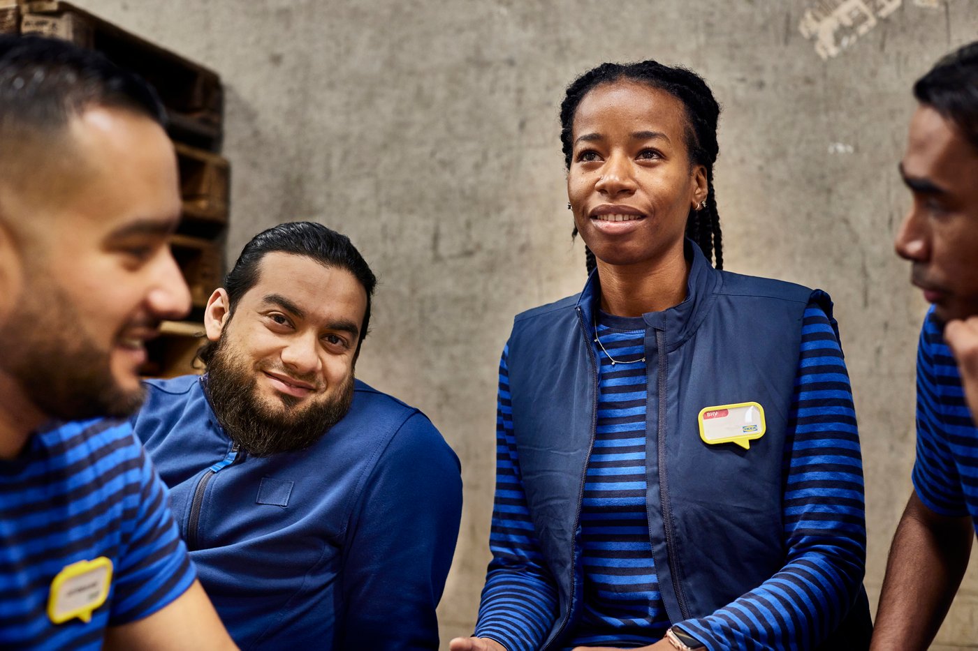 Three IKEA co-workers wearing a blue IKEA uniform, smiling to each other