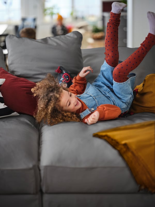 Un enfant vêtu d’une robe en jean et de leggings rouges est allongé sur un canapé gris foncé.