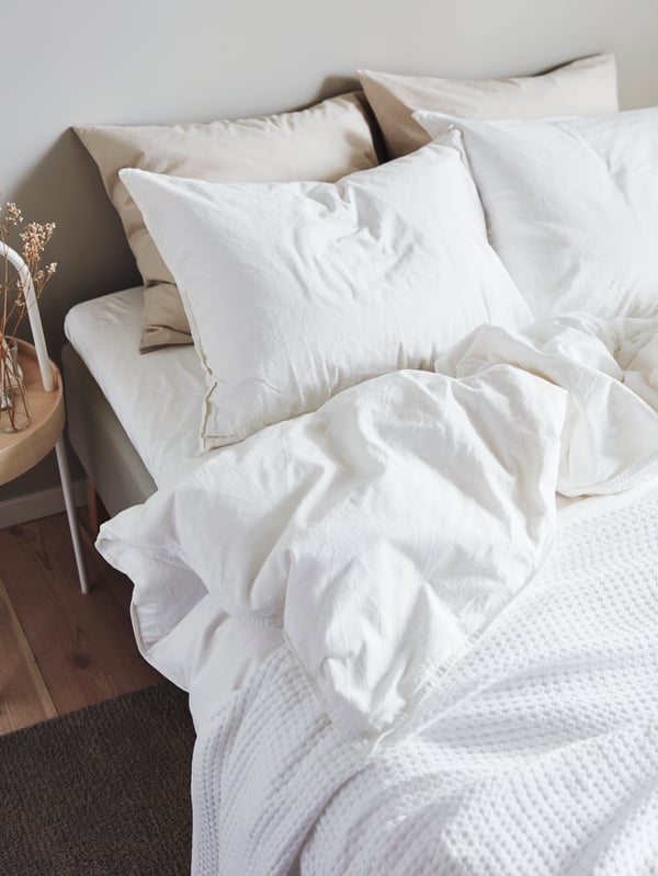 A double bed dressed with white ÄNGSLILJA bed linen, a VÅRELD bedspread and two of four pillows in beige DVALA pillowcases.