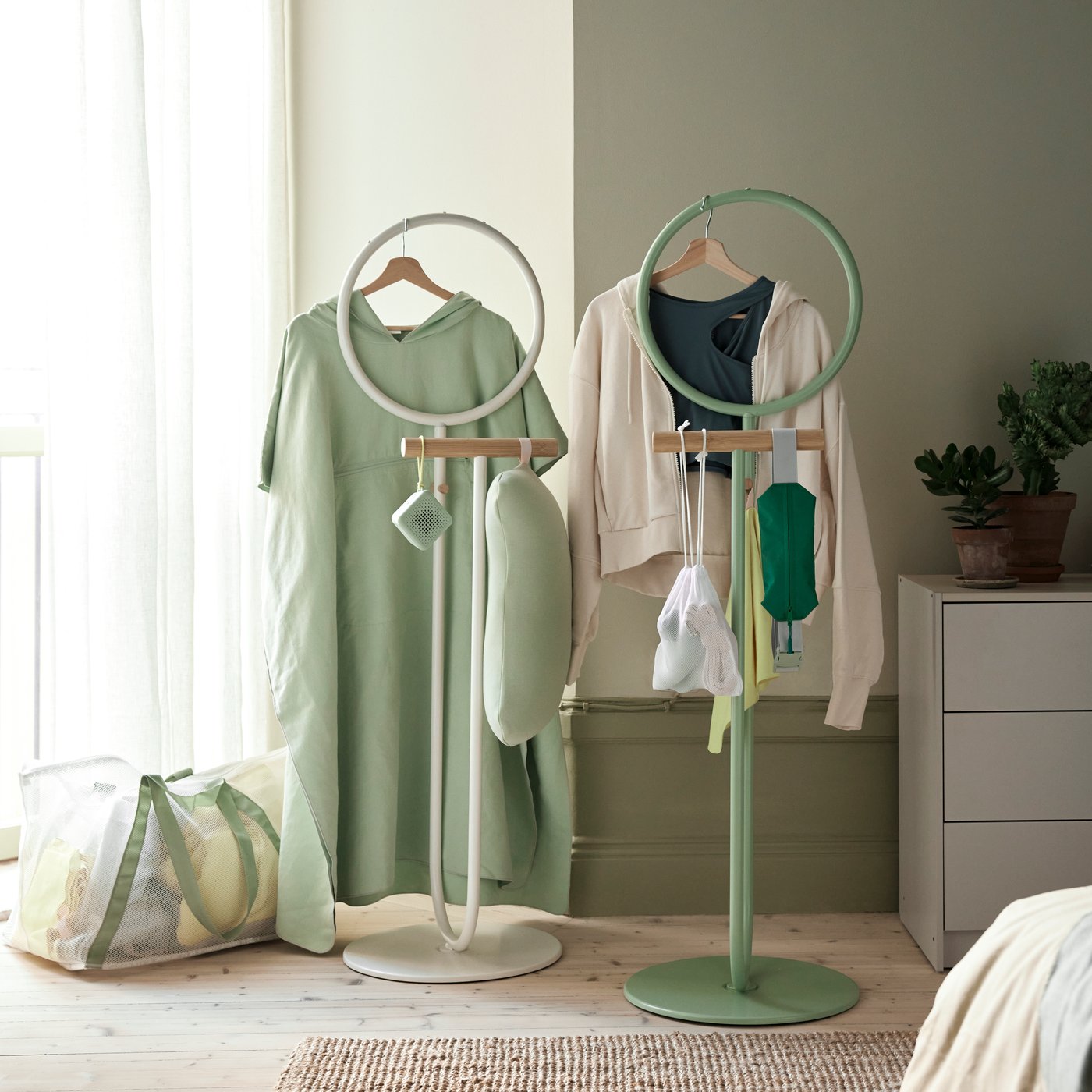 Two DAJLIEN valet stands are in a room, with clothing hanging off them and the DAJLIEN carrier bag on the floor.