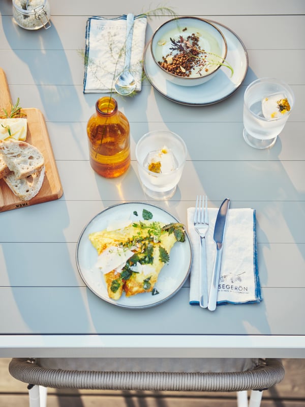 Table champêtre avec vaisselle GLADELIG, deux verres et des serviettes pliées avec logos estampillés.
