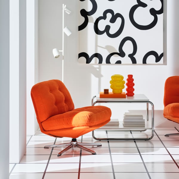 Two orange DYLINGE swivel armchairs are placed next to a coffee table with a yellow and an orange KÄLLARHALS vase on it.
