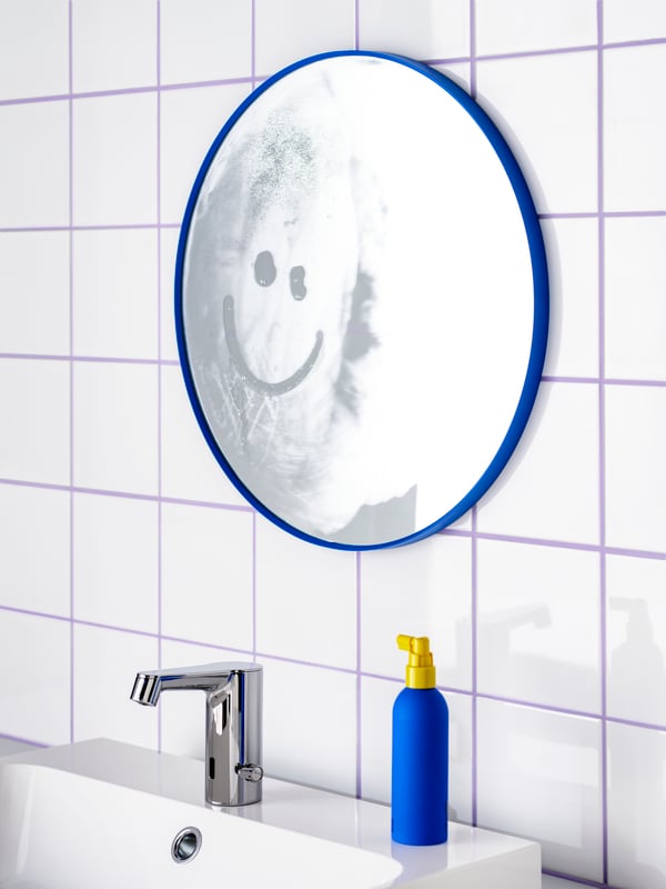 Un miroir LINDBYN bleu fixé au mur au-dessus d’un lavabo. Un smiley a été dessiné sur la surface embuée du miroir.