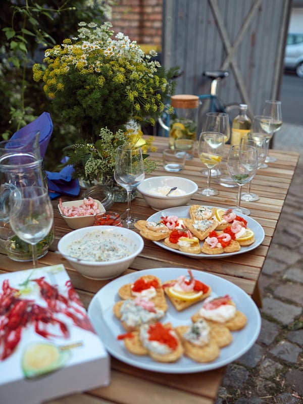 Ett bord utomhus uppdukat med dryck, kräftor och våfflor toppade med räkor.