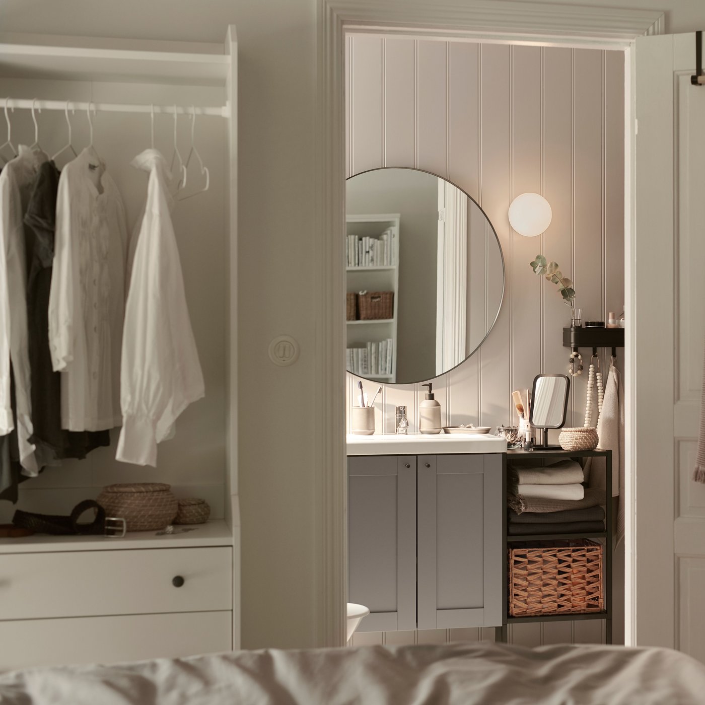 Ein ENHET/TVÄLLEN Waschbeckenschrank mit zwei Türen ist in einem kleinen DIY-Badezimmer mit angrenzendem Schlafzimmer zu sehen.