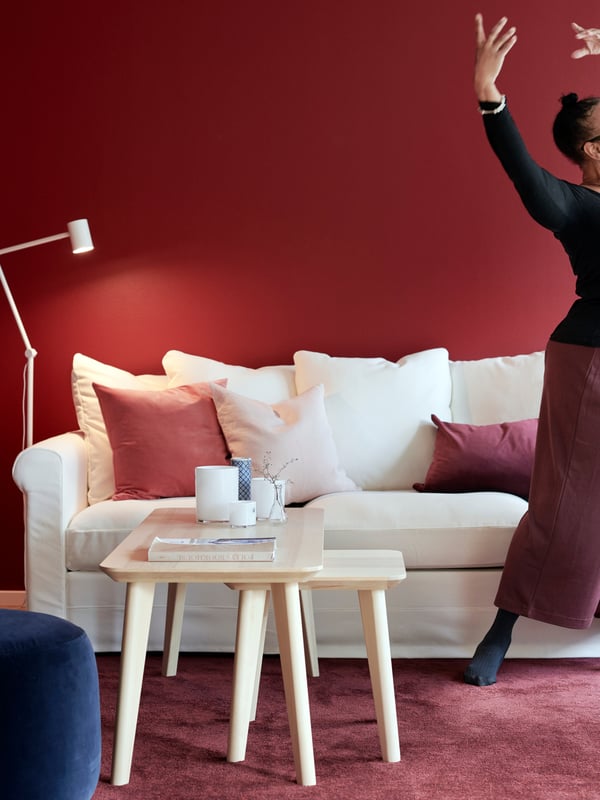 Woman striking a graceful dance pose, standing next to a sofa. White-and-red matching furniture, wall, rug and details.