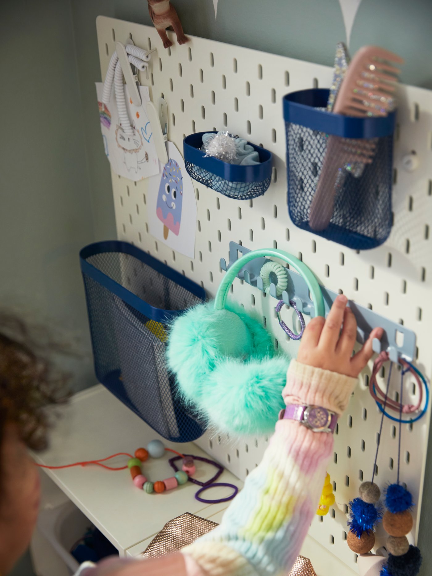 Light blue walls, a child hooking a toy on a white IKEA SKADIS pegboard 