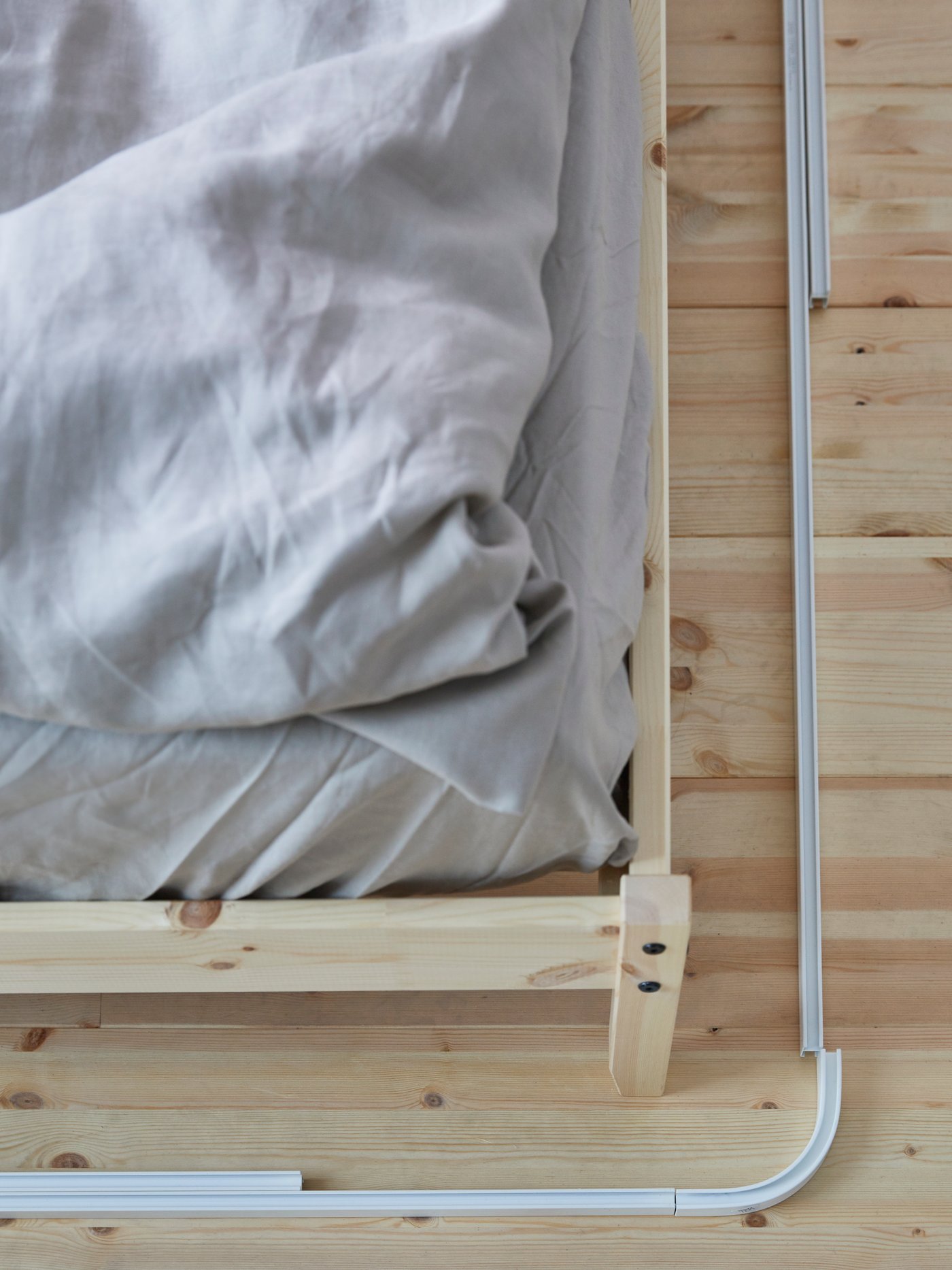 A corner of a bed with VIDGA curtain track rails placed on the floor around the bed to measure them for installation.
