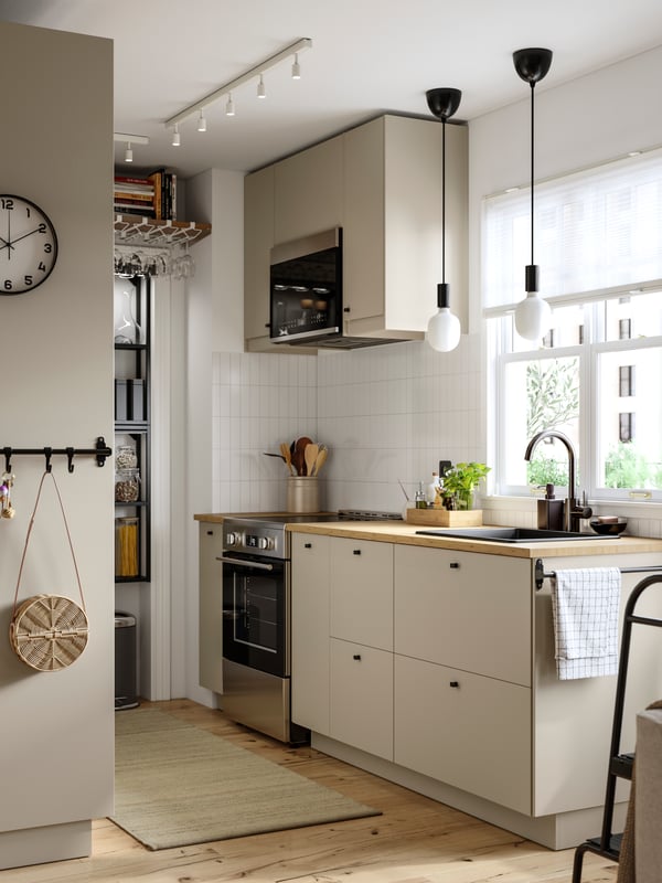 A kitchen has cabinets with beige HAVSTORP fronts, an ENHET wall frame with shelves in anthracite and a rug on the floor.