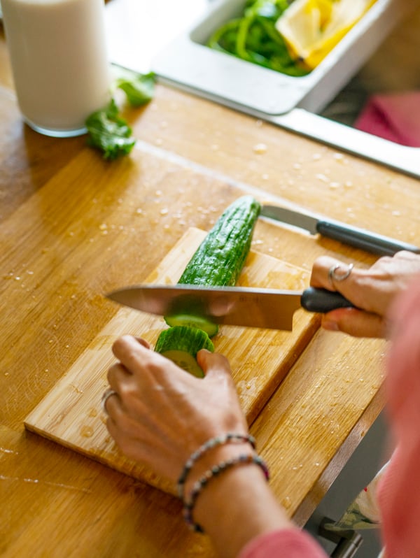 A woman chops a cucumber with a FÖRDUBBLA knife on an APTITLIG chopping board.