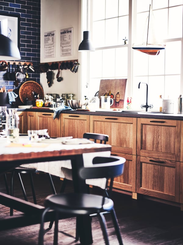 A kitchen with oak VEDHAMN drawer fronts, a worktop, a sink, a table, YNGVAR chairs and a dark grey HEKTAR pendant lamp.