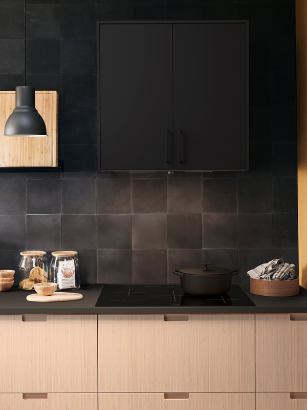 A kitchen cooking area with a MAXIMERA cabinet, a black lamp and a SÄRKLASSIG induction cooktop.