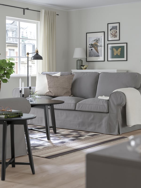 Svetlo siva EKTORP sofa, uramljena slika i udobne dekoracije u modernoj dnevnoj sobi.